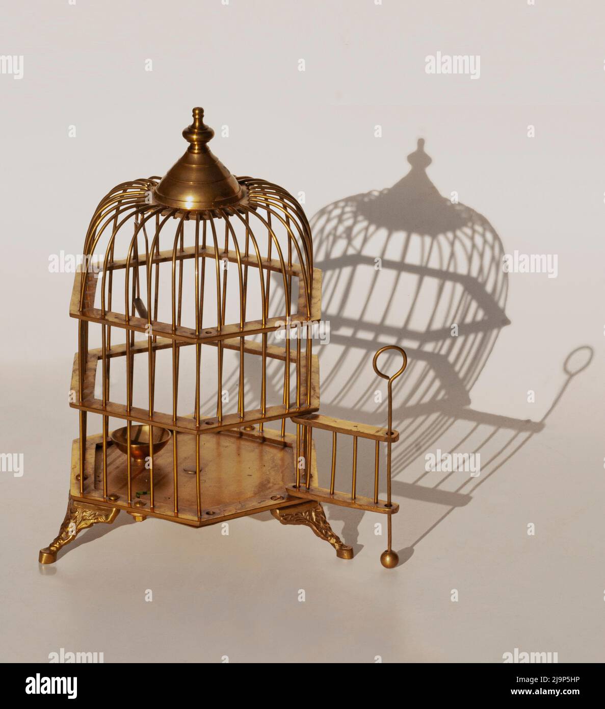 Esta jaula de pájaros de latón es de patas, tiene cinco lados formando un redondo en la parte superior, y una puerta abierta. En el fondo es una sombra agradable de la jaula de pájaros. Foto de stock