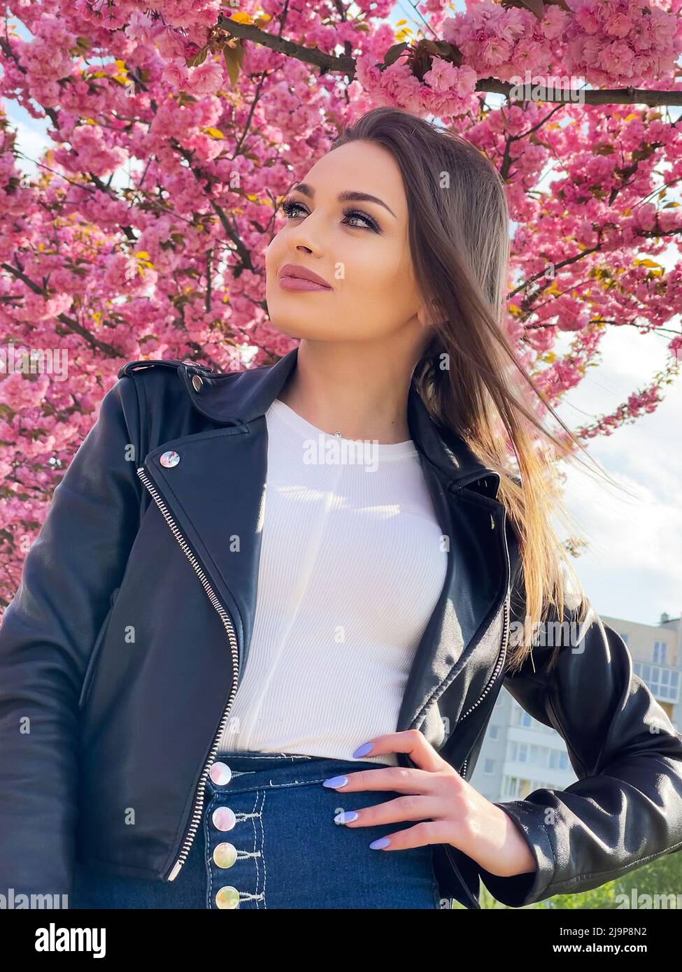 perderse por qué Dificil Hermosa mujer joven vestida de chaqueta negra, de color sakura flores en  primavera Fotografía de stock - Alamy