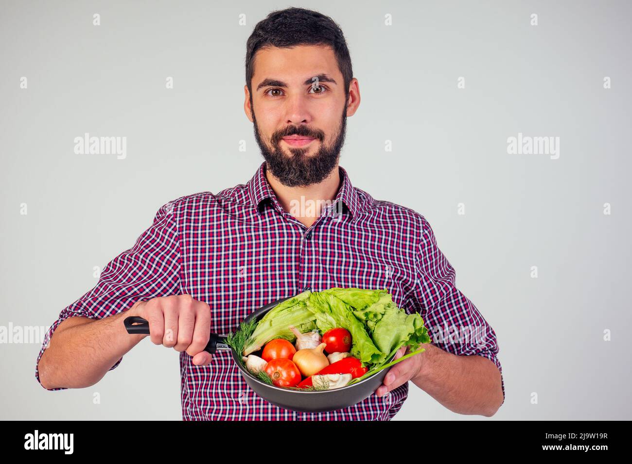 Concepto de comida sana y vegana. Hombre barbudo negro a cuadros en ensalada de cocina con tomates, pepino, champiñones, cebolla y ajo Foto de stock