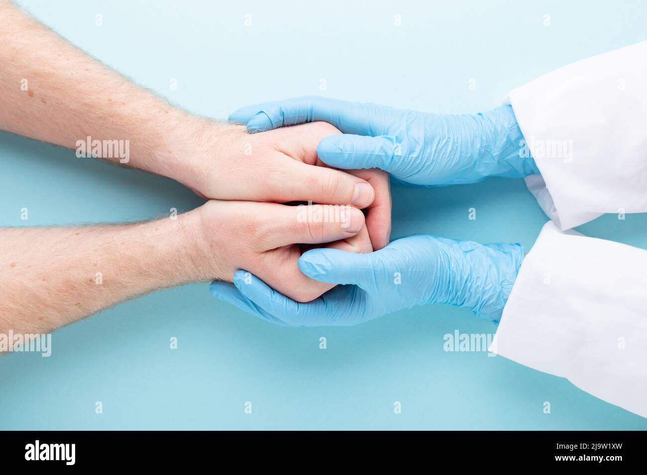 Las manos del doctor en guantes médicos que sostienen las manos del hombre. Foto de stock
