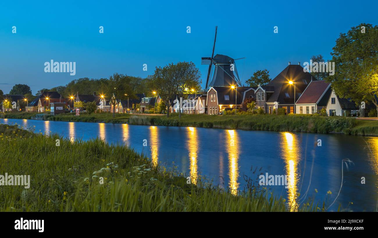 Típico pueblo holandés tradicional con granjas y molino de viento a lo largo del canal en el crepúsculo, Alkmaar, Holanda Septentrional, Holanda. Foto de stock