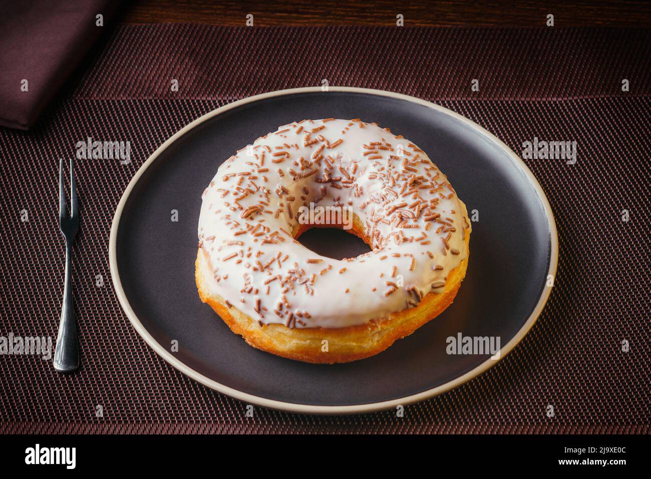 Sabroso donut aislado en un plato sobre una mesa fina. Donuts, con chocolate blanco rociado con virutas de chocolate, pasteles finos Foto de stock