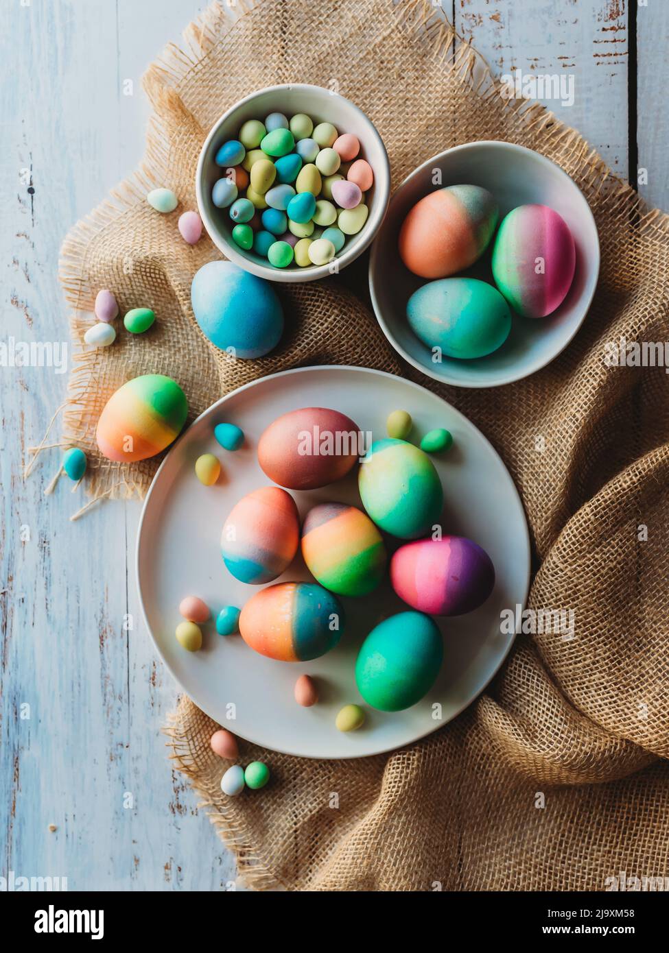 Surtido de huevos de Pascua de colores brillantes sobre madriguera y madera blanca. Foto de stock