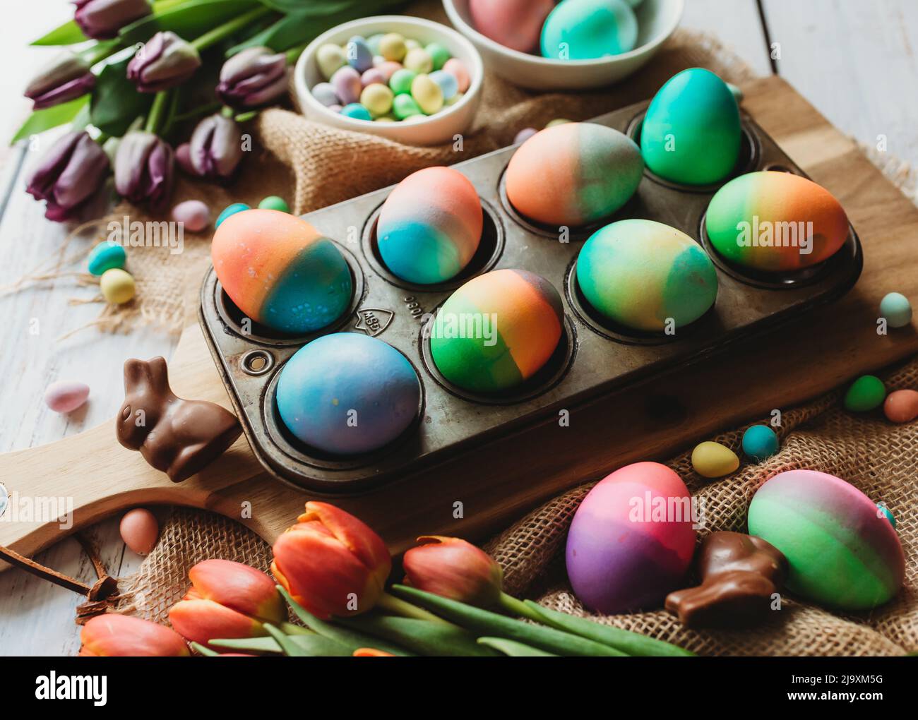 Bandeja de huevos de Pascua de colores brillantes rodeada de tulipanes. Foto de stock