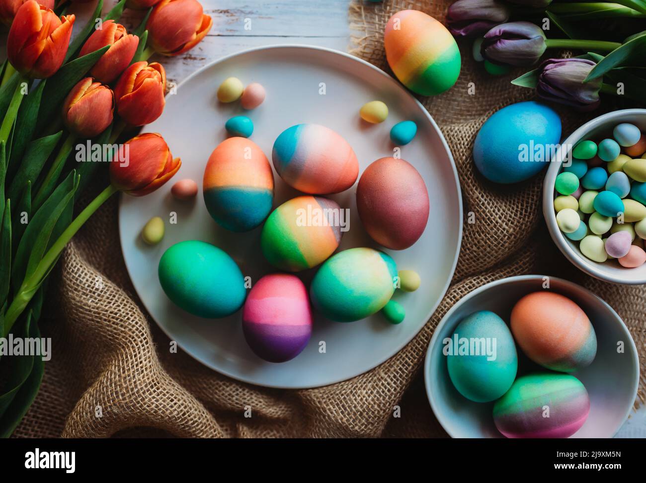 Surtido de huevos de Pascua de colores brillantes rodeados de tulipanes. Foto de stock