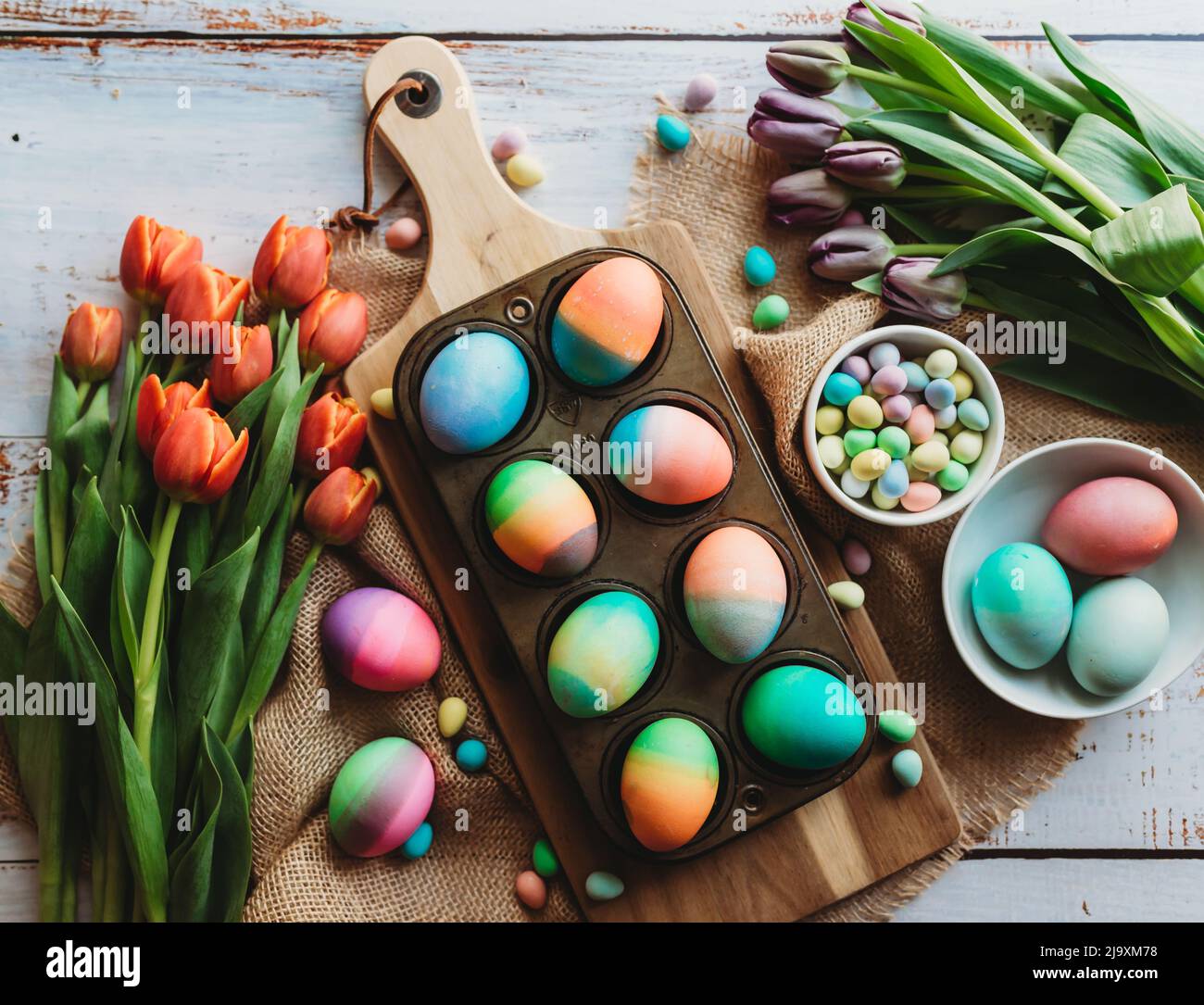 Bandeja de huevos de Pascua de colores brillantes rodeada de tulipanes. Foto de stock