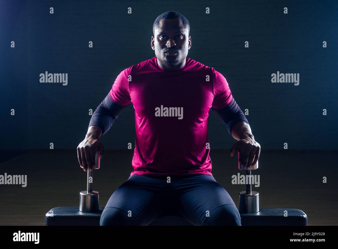 hombre afroamericano musculoso haciendo ejercicios de flexiones con pesas en el gimnasio sobre un fondo negro Foto de stock