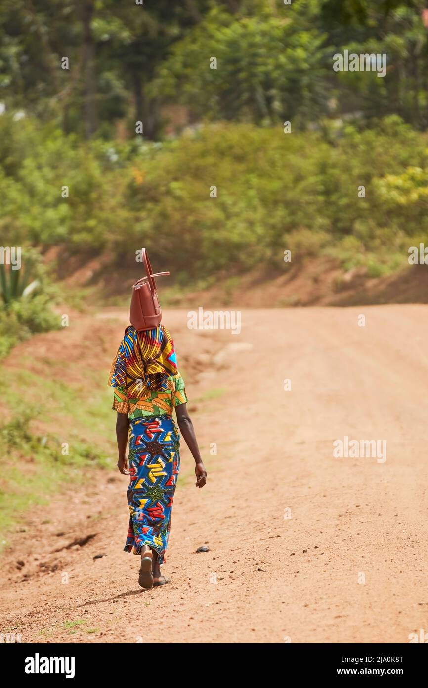 Una mujer africana con un colorido paño tradicional kanga lleva una bolsa sobre su cabeza, Arusha, Tanzania, África. Foto de stock