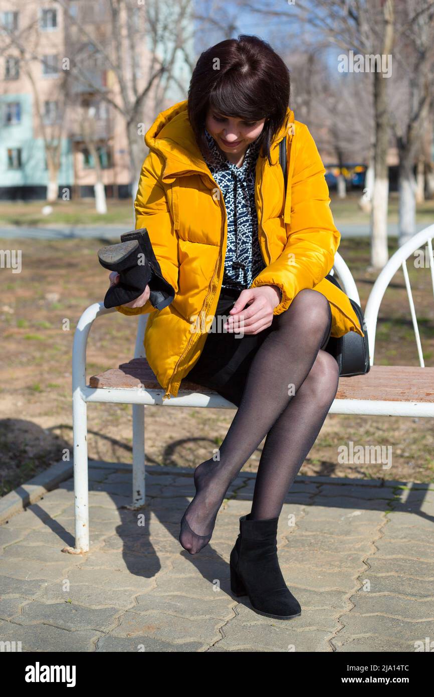 Una mujer morena con una chaqueta amarilla brillante se sentó en el banco  del parque para sacudir una piedra que se metió en sus zapatos Fotografía  de stock - Alamy