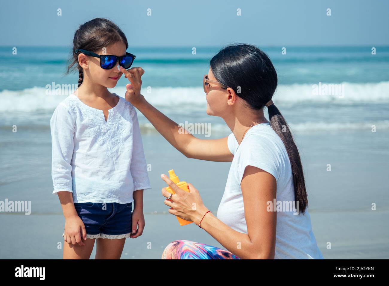 madre e hija aplican crema en la playa Foto de stock