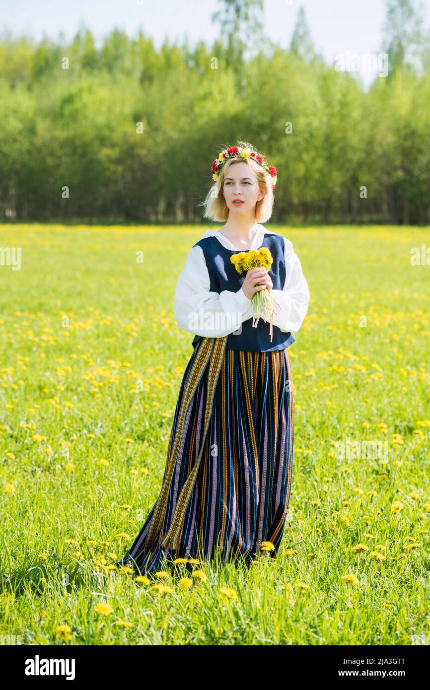 Mujer joven con ropa nacional con corona amarilla de diente de león en  campo primaveral. Ligo Fotografía de stock - Alamy