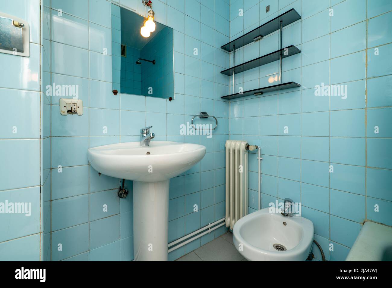 Baño con espejo con balda de cristal lavabo de porcelana con pie del mismo  material radiador pequeño de aluminio blanco y salida a pasillo