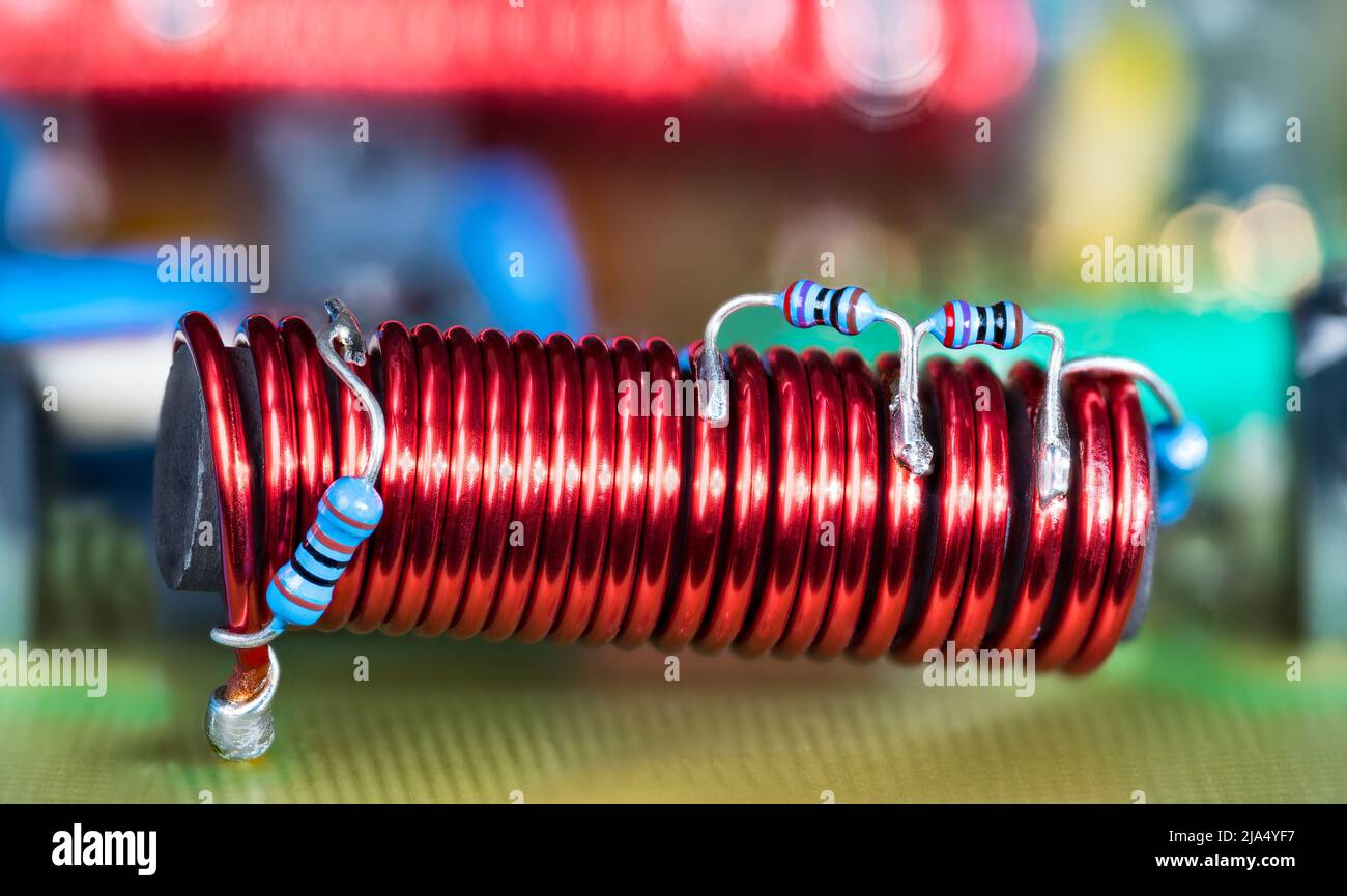 Bobina electrónica: Núcleo de ferrita y resistencias con código de color pequeño azul en cable de cobre rojo. Inductor electromagnético cilíndrico. Detalle de PCB del amplificador de TV por cable. Foto de stock