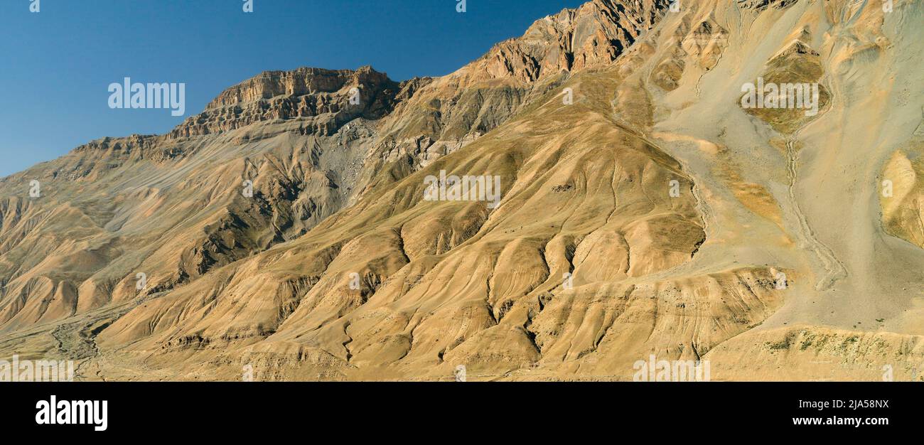 Vista panorámica de las montañas del Himalaya con crestas rocosas y pendientes escarpadas bajo cielo azul en verano cerca de Kaza, Himachal Pradesh, India. Foto de stock