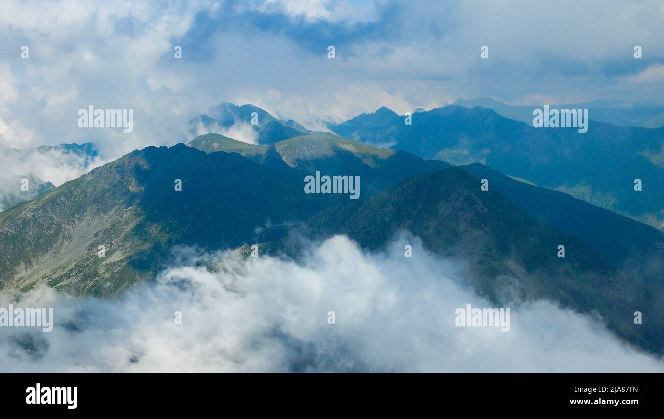 Vista desde el Pico de la Montaña Negoiu. Cielo dramático con nubes y niebla cubriendo la montaña escarpada y escarpada crestas rocosas. Temporada de verano, Cárpatos, Rumania. Foto de stock