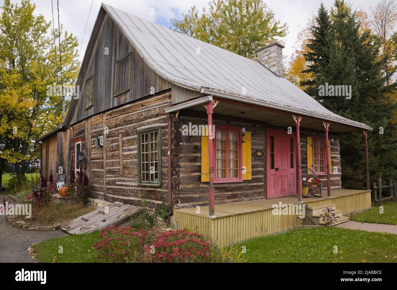 Antigua casa de madera estilo cabaña de alrededor de 1825 Canadiana con techo de chapa galvanizada en otoño. Foto de stock