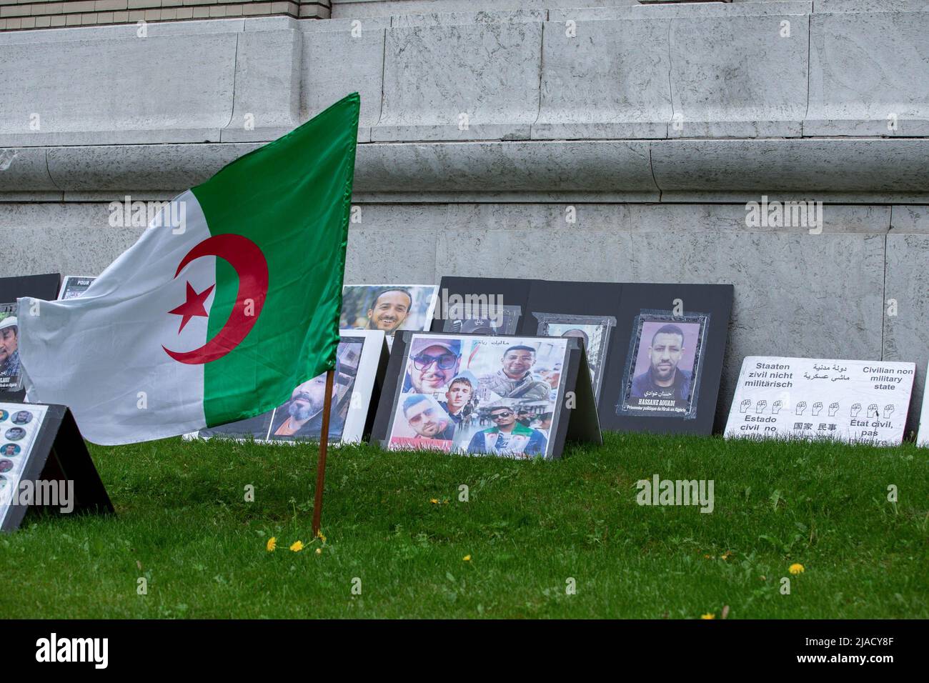 Una bandera argelina y tarjetas con fotos y nombres de presos políticos en Argelia se colocan en el césped para que los que se desvíen vean durante la protesta. Cuatro años después de la diáspora argelina, el movimiento Hirak sigue luchando por la democracia en Montreal. Organizado por Tous unis pour notre Algerie, cientos de manifestantes se reunieron frente al Consulado de Argelia para exigir la retirada de los actuales líderes políticos, encabezados por el presidente Abdelmadjid Tebboune. Citando la corrupción crónica y la falta de resoluciones previsables, los manifestantes llamaron al gobierno un gobierno mafioso. (Foto de Giordanno Br Foto de stock
