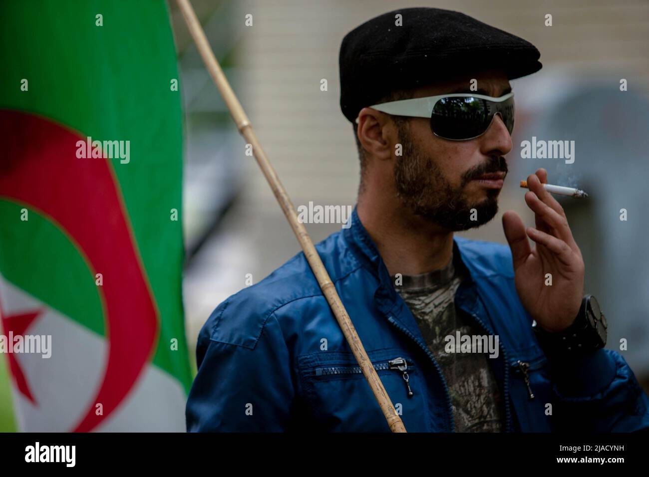 Un manifestante argelino sostiene la bandera argelina mientras fuma un cigarrillo durante la protesta. Cuatro años después de la diáspora argelina, el movimiento Hirak sigue luchando por la democracia en Montreal. Organizado por Tous unis pour notre Algerie, cientos de manifestantes se reunieron frente al Consulado de Argelia para exigir la retirada de los actuales líderes políticos, encabezados por el presidente Abdelmadjid Tebboune. Citando la corrupción crónica y la falta de resoluciones previsables, los manifestantes llamaron al gobierno un gobierno mafioso. (Foto de Giordanno Brumas/SOPA Images/Sipa USA) Foto de stock