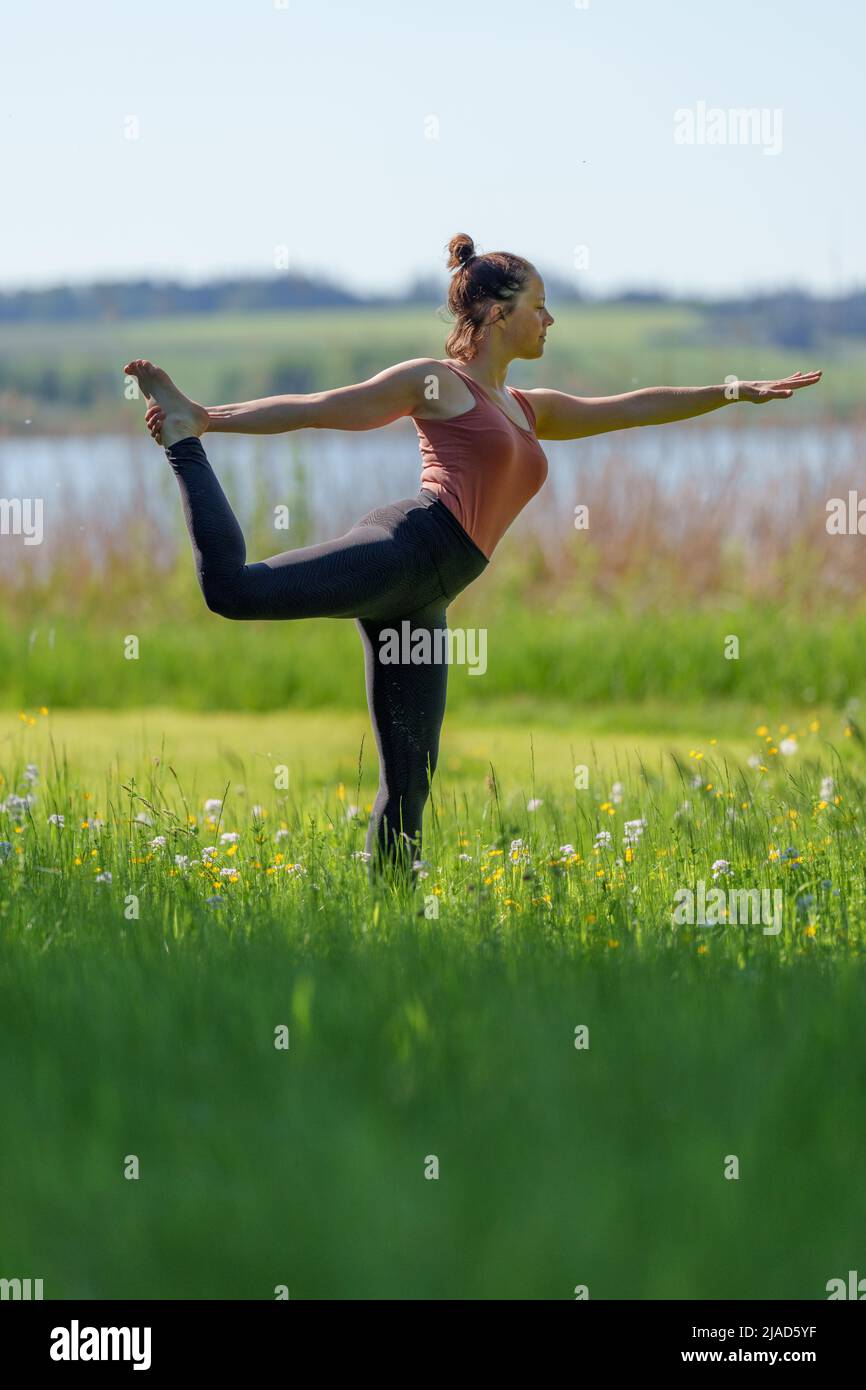 Mujer de pie en una pierna haciendo pose bailarina por Wallersee, Salzburgo, Austria Foto de stock