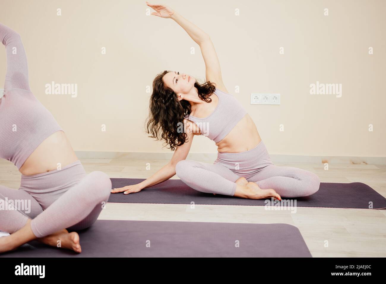 Mujer deportiva de mediana edad, monitor de en ropa deportiva rosa estirando y pilates sobre colchoneta de yoga en el estudio con espejo Fotografía de -