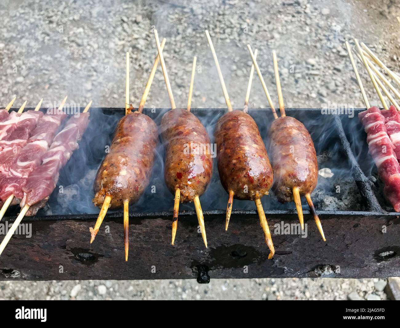 Apetitosas salchichas y brochetas de carne a la parrilla mientras cocinan al aire libre durante una barbacoa Foto de stock
