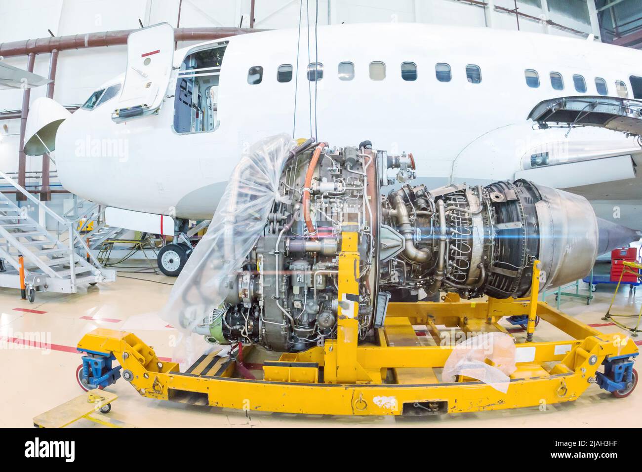 Primer plano del motor de aviones turboventiladores de alta derivación cerca de un avión de pasajeros en un hangar Foto de stock