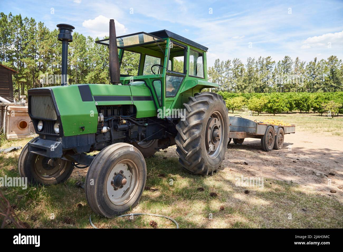 Tractor verde junto a un campo naranja durante el verano, imagen representativa de la agricultura y el mundo rural. Foto de stock