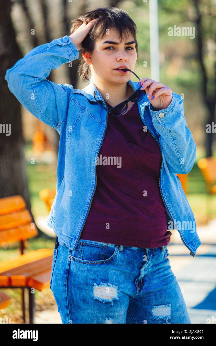 Hermosa chica con pelo corto negro en su 20s en parque con jeans azul claro y una chaqueta vaquera azul claro Fotografía de stock - Alamy