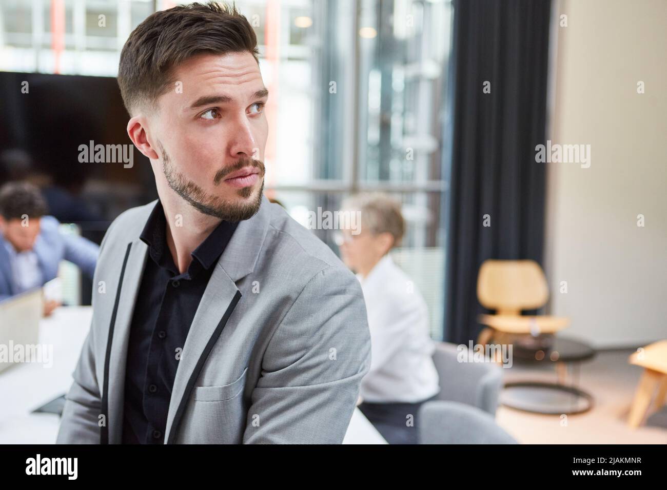 Joven hombre de negocios mirando al hombro con escepticismo y cuestionamiento en la reunión en el cargo Foto de stock
