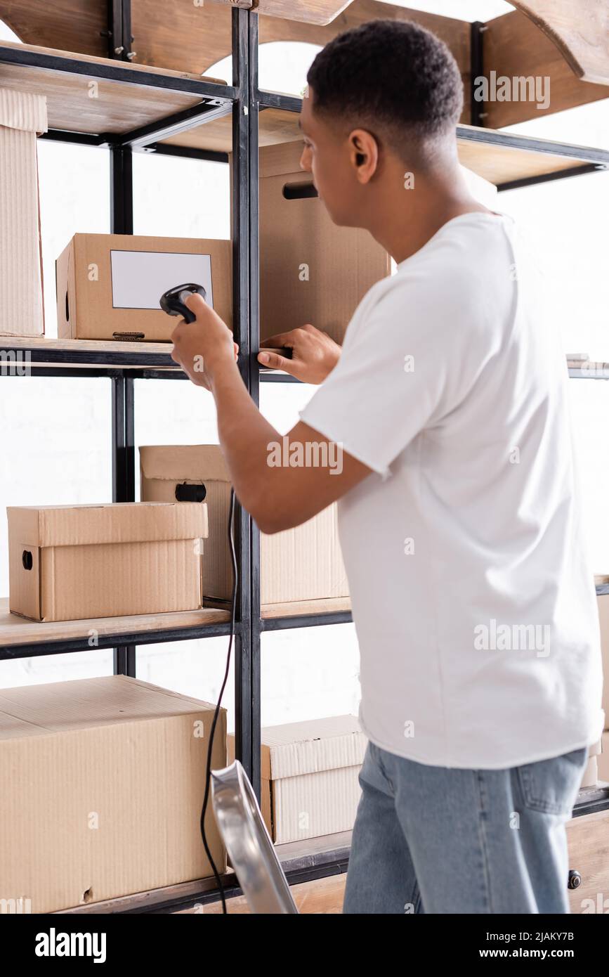 Vista lateral del propietario de la tienda web en línea afroamericana escaneando paquetes en rack Foto de stock