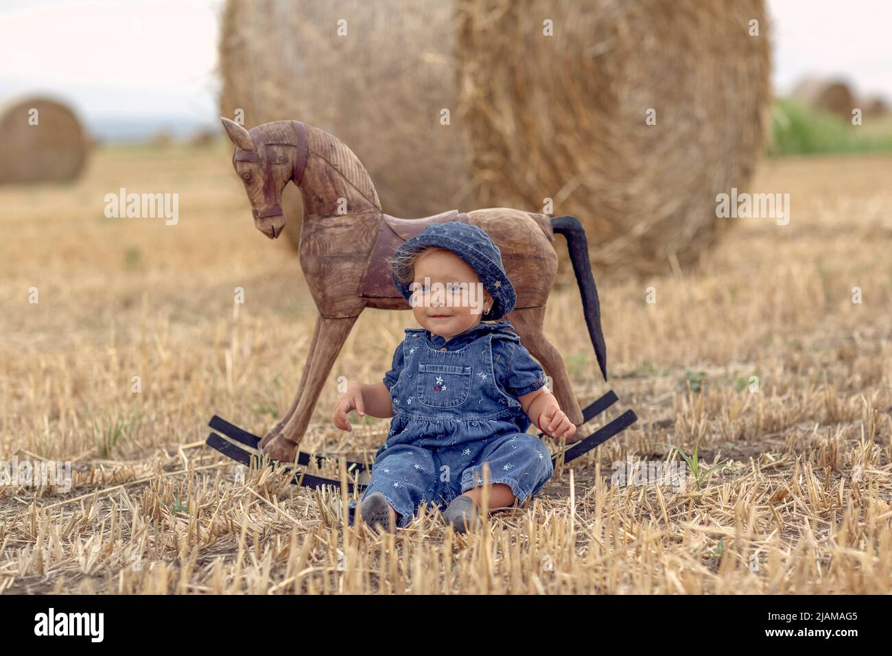 Feliz linda chica en el campo de trigo con caballo mecedora.Naturaleza en el país Foto de stock