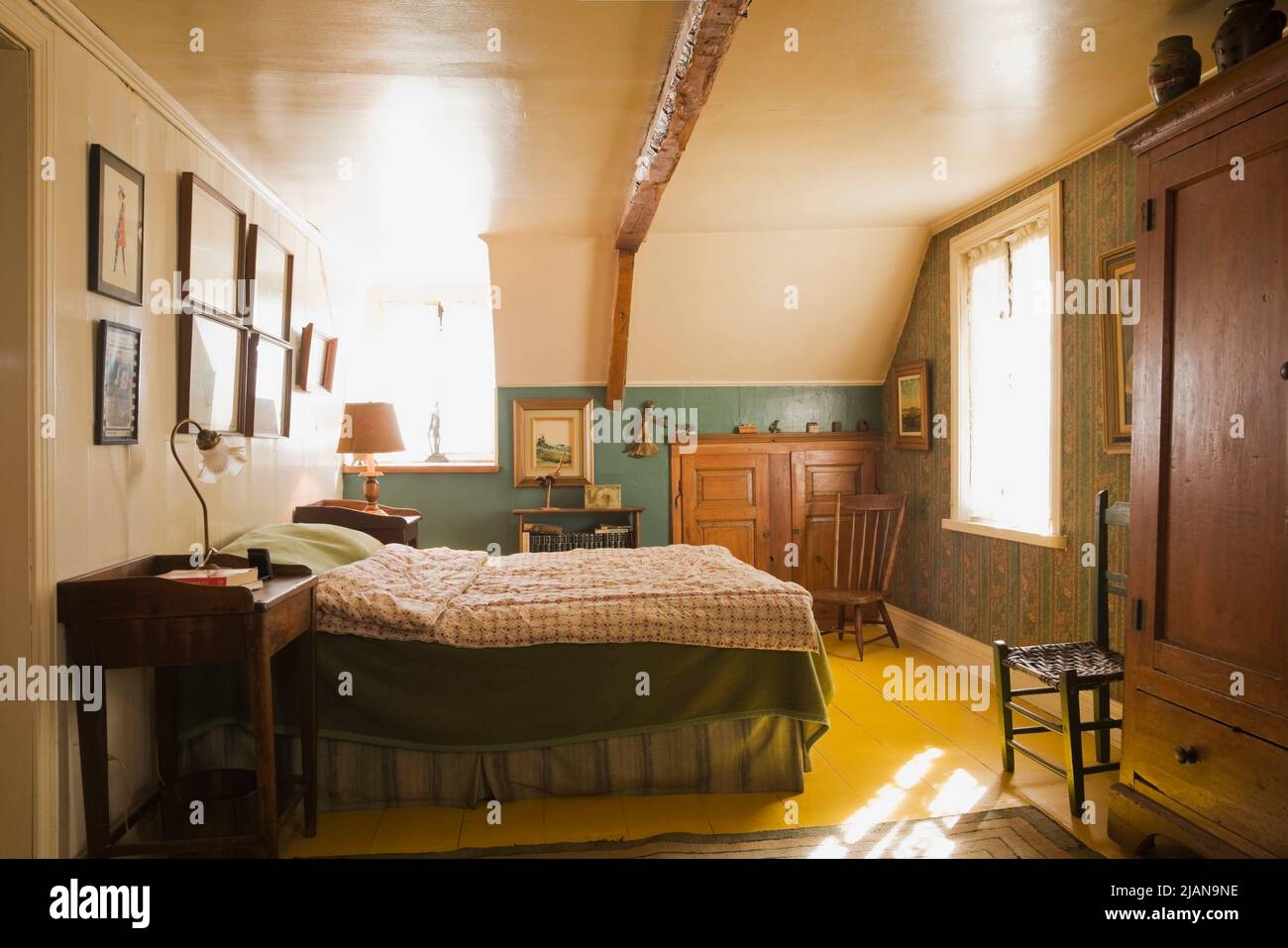 Cama doble con cubrecama de cuadros y muebles antiguos en el dormitorio  principal en el piso de arriba dentro de la antigua casa estilo cabaña de  alrededor de 1810 Canadiana Fotografía de