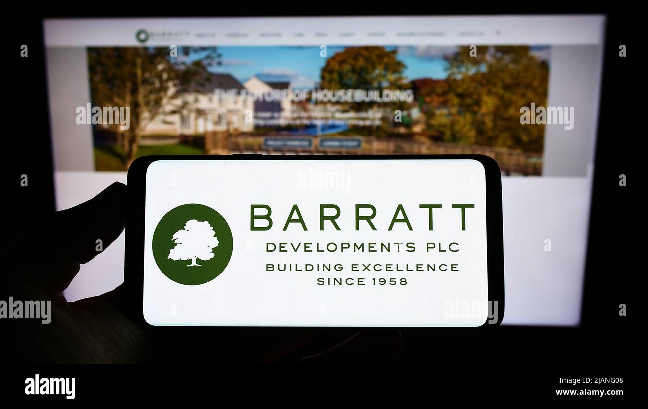 Persona con smartphone con el logotipo de la empresa inmobiliaria Barratt Desarrolloments plc en la pantalla frente al sitio web. Enfoque en la pantalla del teléfono. Foto de stock