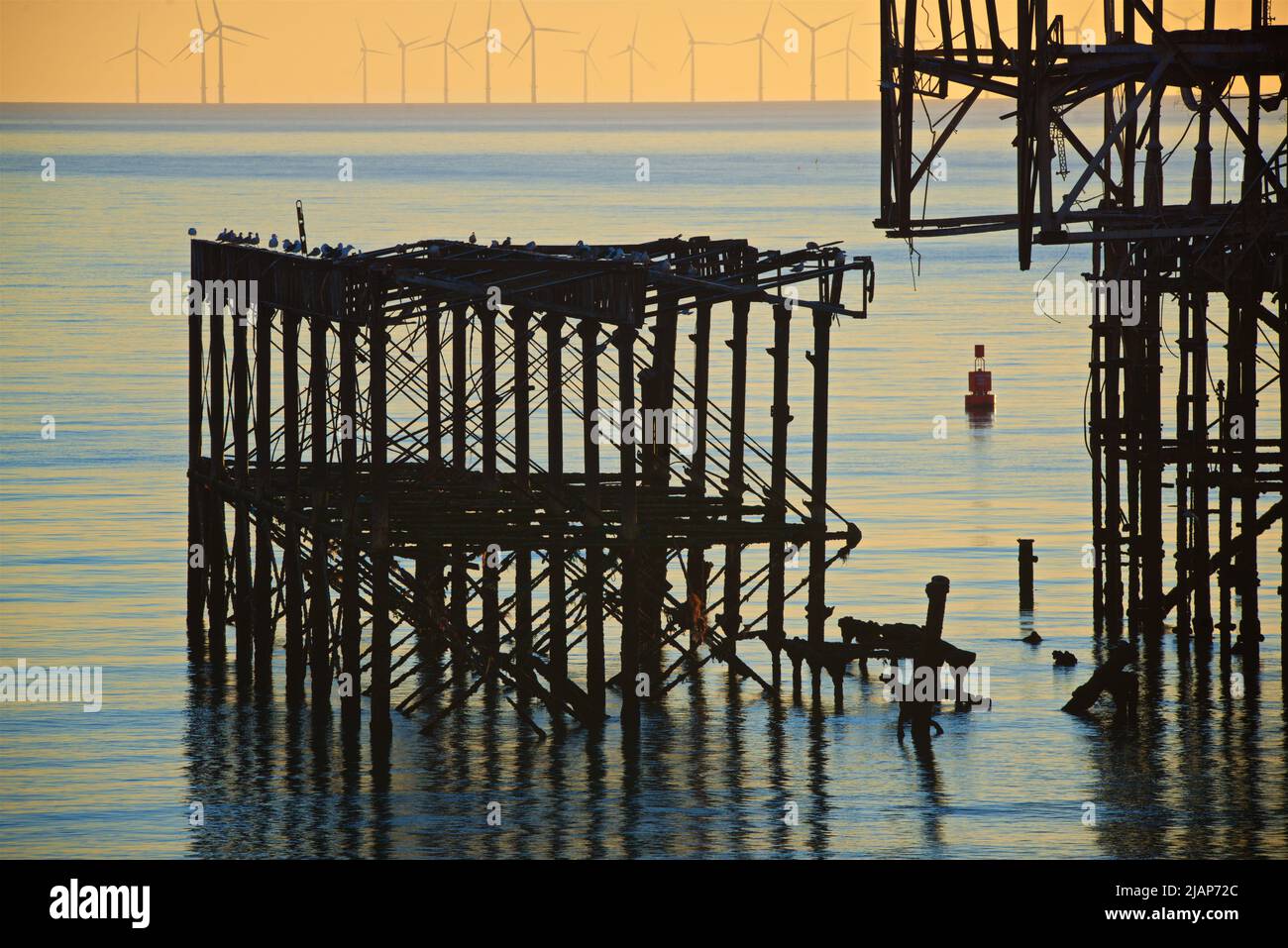 Detalle de la estructura de hierro derelicta y desintegradora del West Pier al atardecer, Brighton. Construido en 1866 y cerrado en 1975, el muelle sigue catalogado como Grado I y es un monumento bien conocido. El parque eólico marino Rampion se puede ver en el horizonte. Las aves marinas se sientan en el muelle Foto de stock