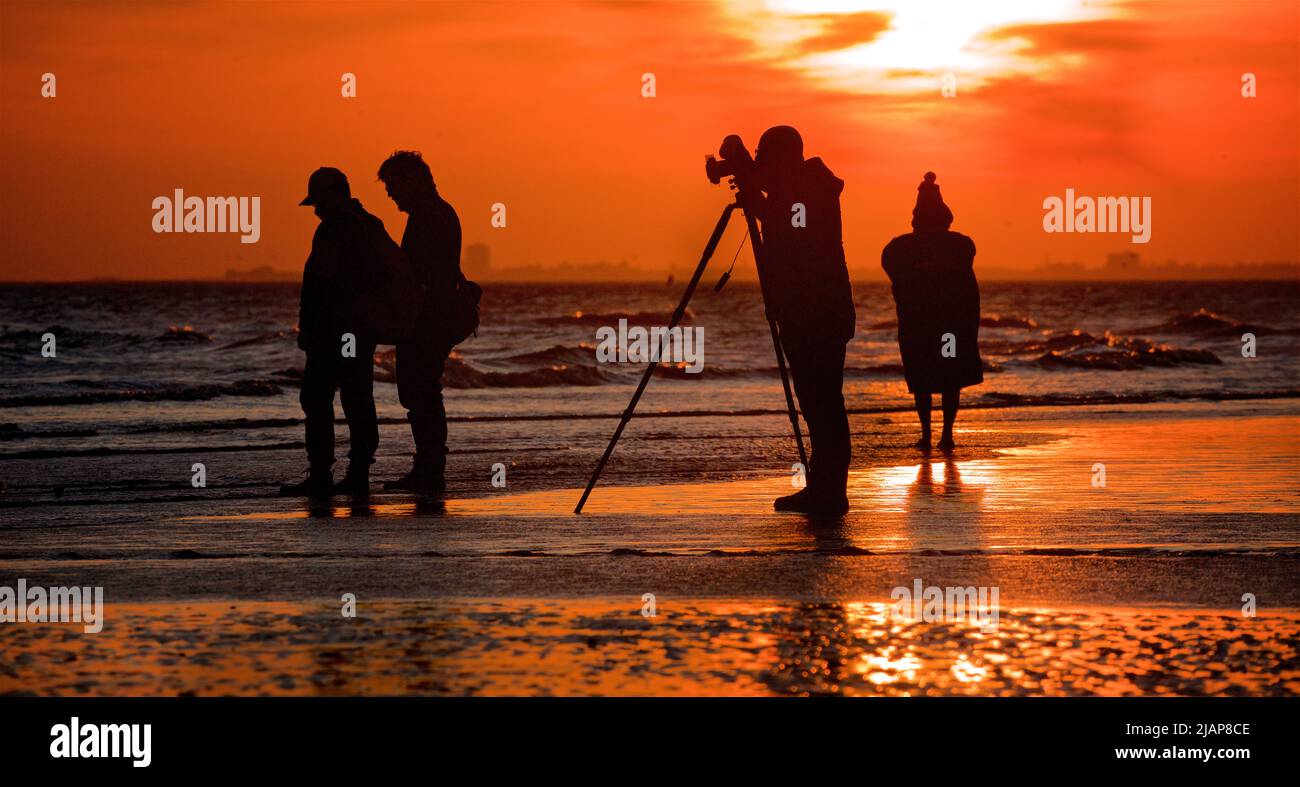 Siluetas de personas en la playa en marea baja, Brighton & Hove, East Sussex, Inglaterra, Reino Unido. Fotógrafo con cámara en trípode. Foto de stock