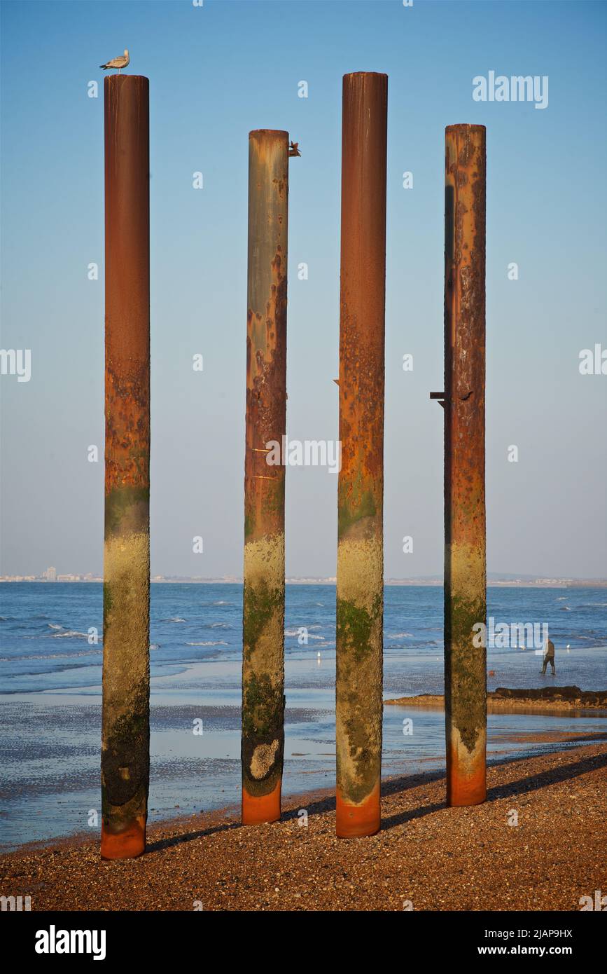 Cuatro pilares verticales de hierro se elevan desde la playa en el sitio de la estructura histórica del West Pier, que se convirtió en abandonado y perdido después de que fue cerrado en 1975. Marea baja. Brighton, East Sussex, Inglaterra, Reino Unido. Worthing en el horizonte distante. Foto de stock