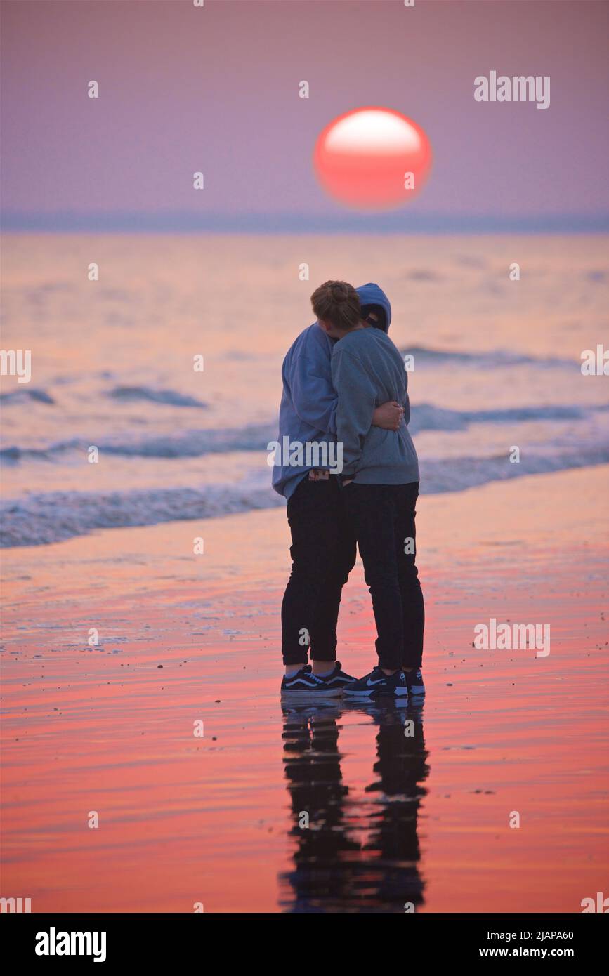 Una pareja cariñosamente abrazada en la playa en marea baja, Sunset, Brighton, Inglaterra, Reino Unido. Foto de stock