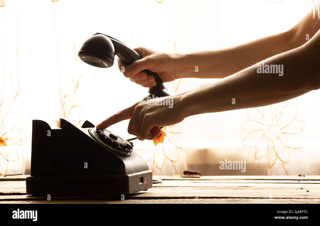 La mano de una mujer marca un número de teléfono en un teléfono viejo en casa en la mesa, un teléfono retro es negro, una llamada Foto de stock