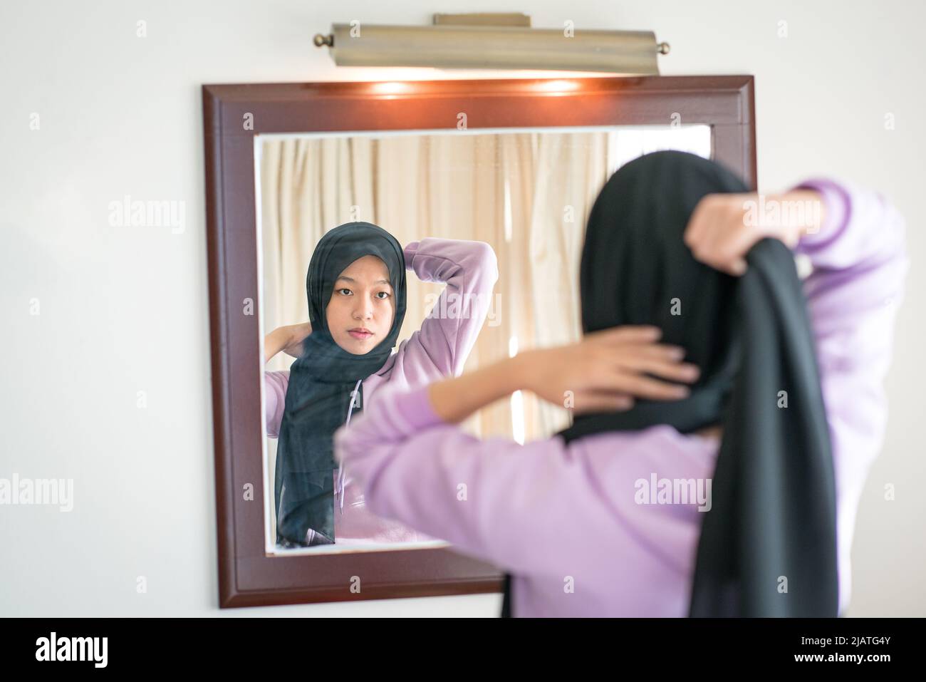 Reflexión sobre un espejo de pared de una mujer musulmana que lleva su pañuelo en la cabeza. Foto de stock