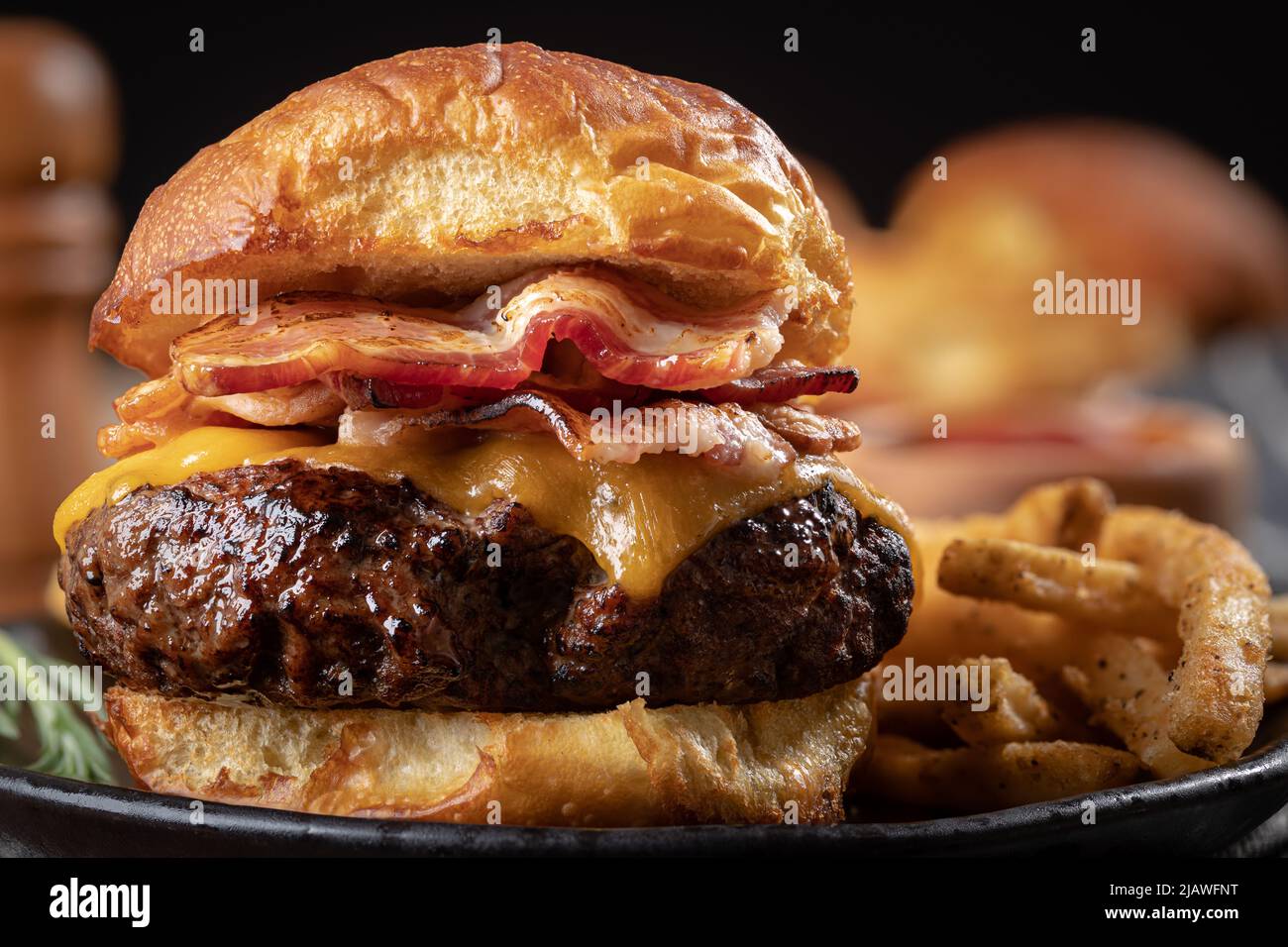 Cierre de una hamburguesa de queso con tocino en una bolita tostada con patatas fritas en un plato Foto de stock