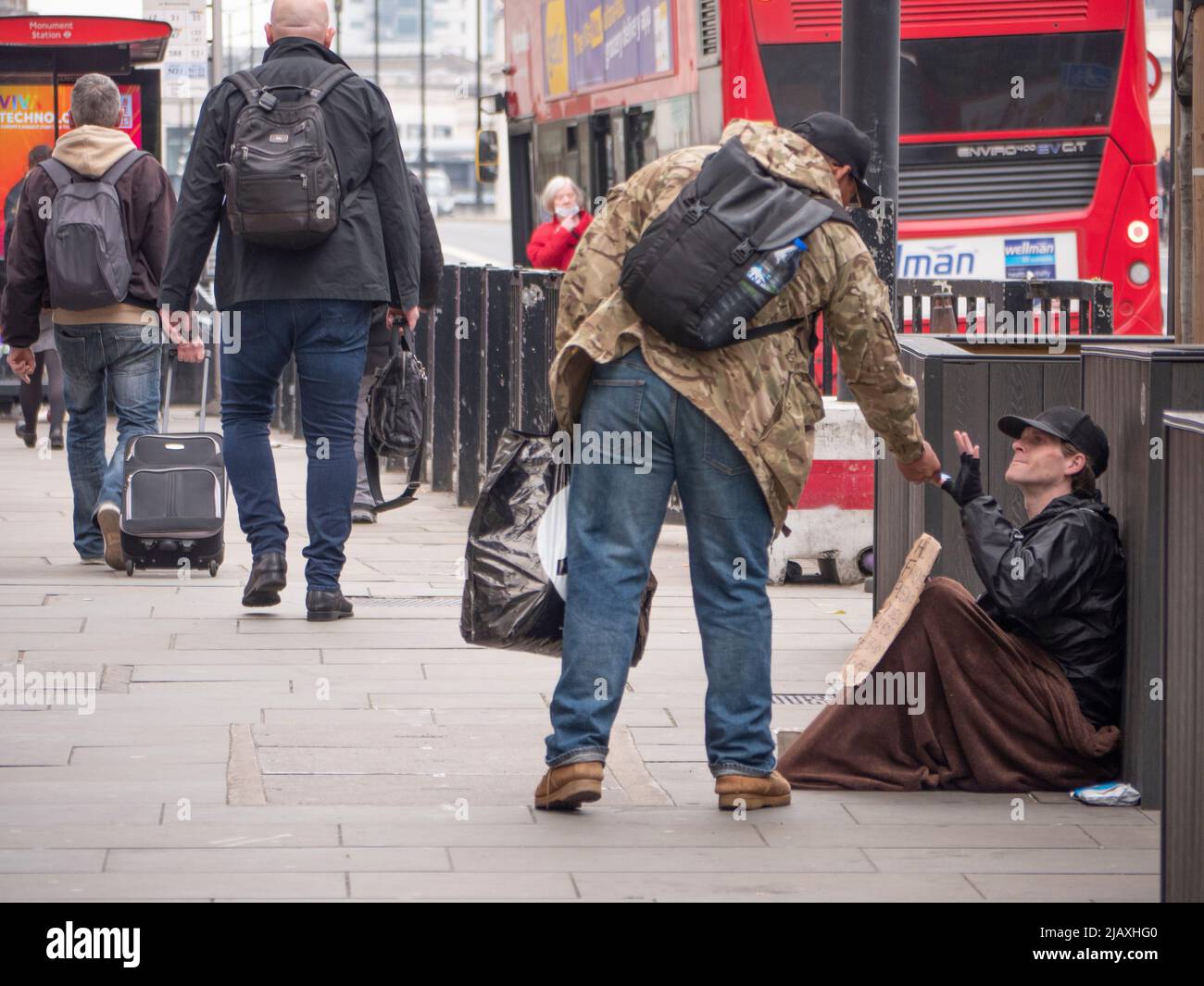 La pobreza en Londres, miembro del público que se inclina para dar alimentos a un mendigo en el Puente de Londres con manta y signo Foto de stock