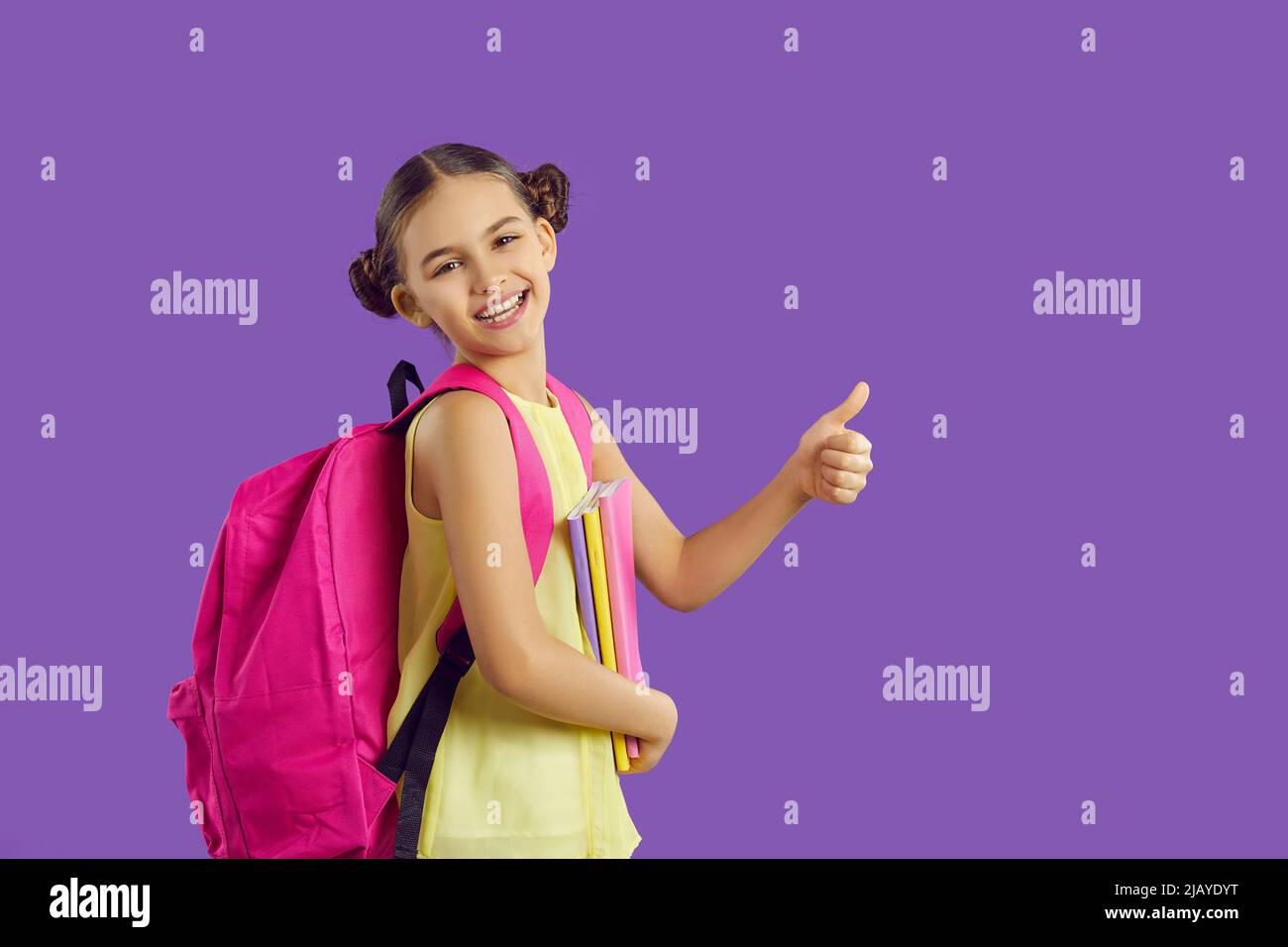 Adorable niña de 5-6 años con mochila rosa, sosteniendo libro de texto y  mostrando el pulgar hacia arriba mirando a la cámara. Maqueta Fotografía de  stock - Alamy