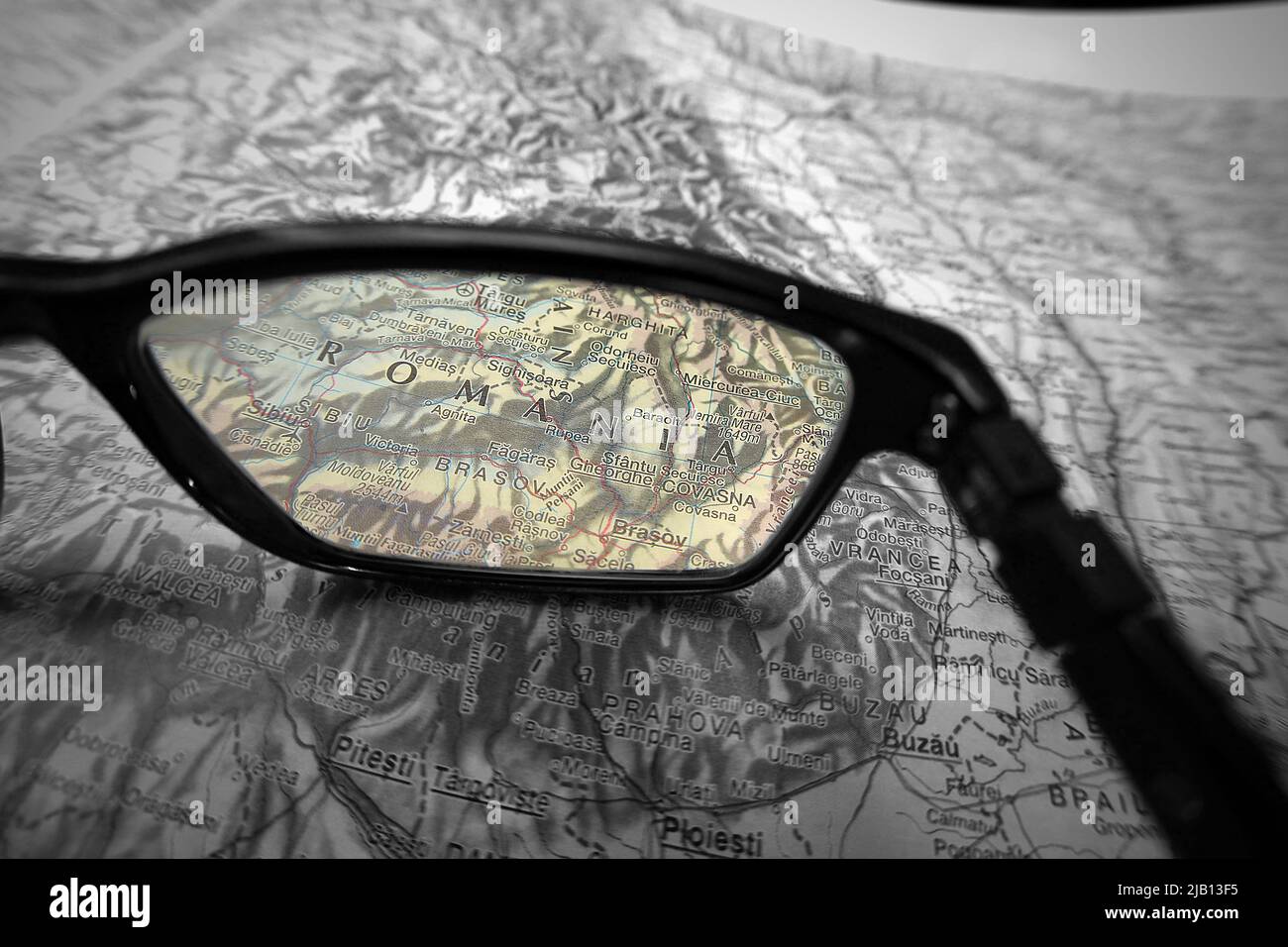 Una imagen ilustrativa creativa que muestra al país de Rumanía en un mapa a través de la lente de las gafas de lectura. El área alrededor de la palabra Rumanía en color Foto de stock