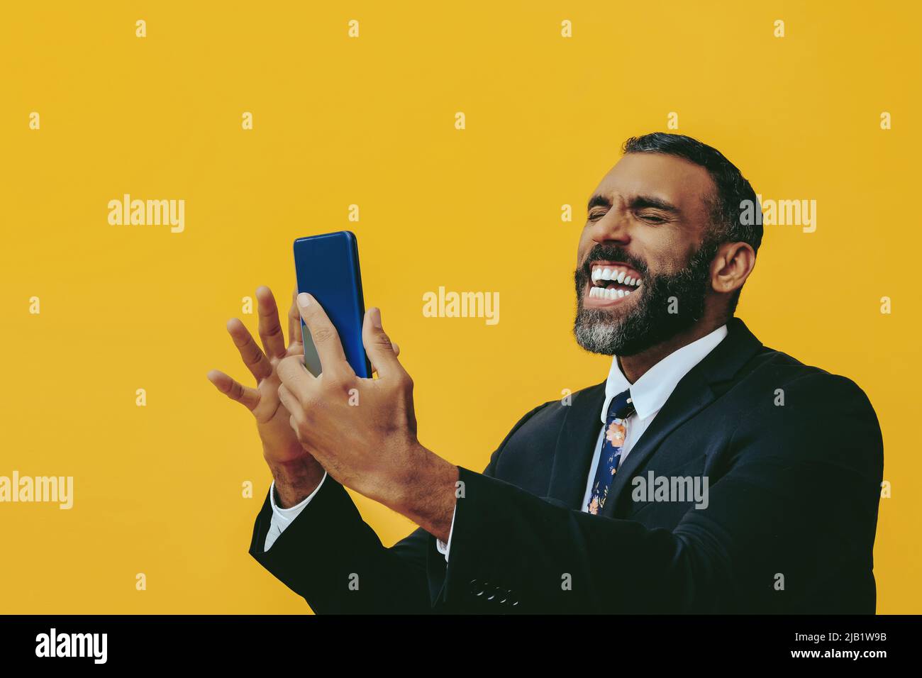 retrato de expresivo enojado con barba hombre en traje y corbata con smartphone videollamada mano sobre amarillo estudio de fondo Foto de stock