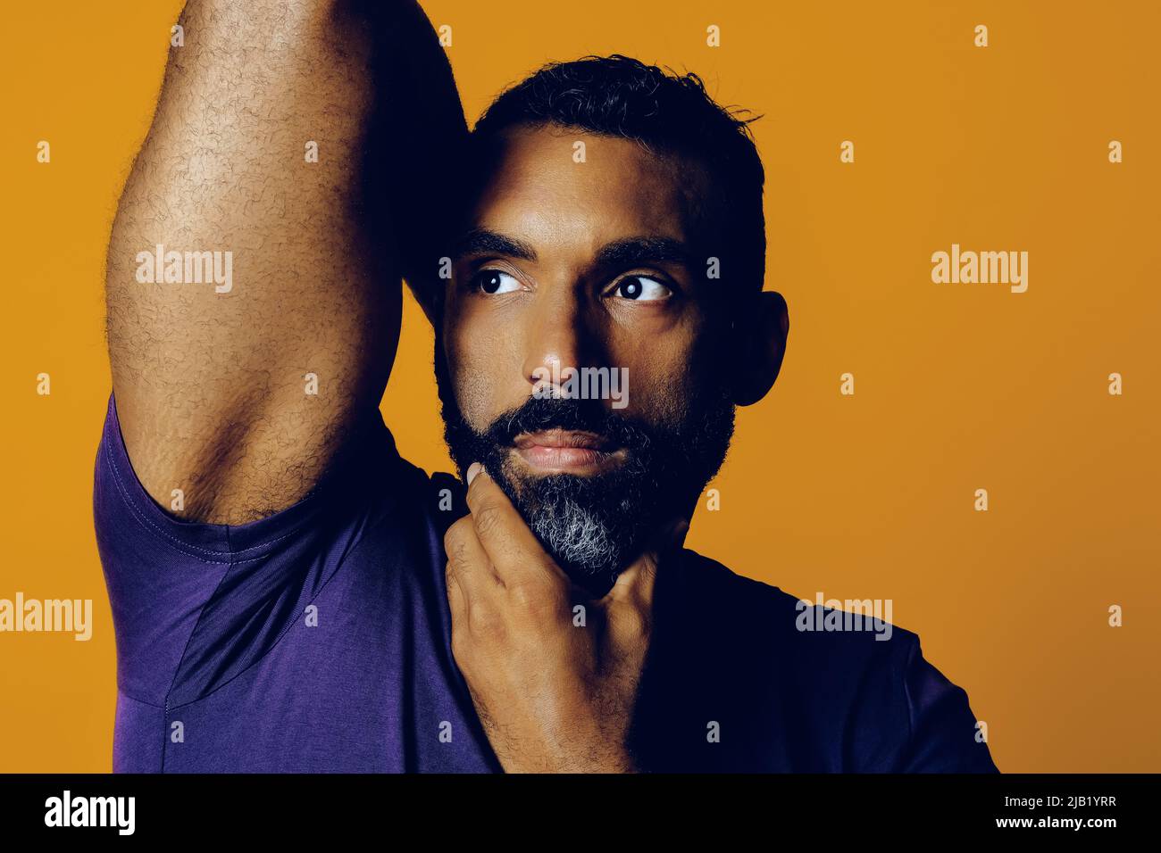 primer plano de un hombre adulto sensible con barba y una mano de bigote en la barbilla mirando hacia el estudio amarillo del espacio de copia Foto de stock