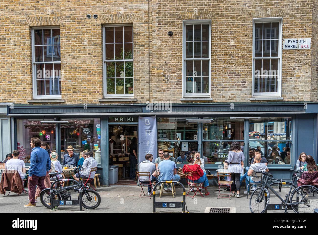 La gente sentada fuera de Briki, una tienda de delicatessen y café y una cervecería de café en Exmouth Market, Clerkenwell, Londres EC1 Foto de stock