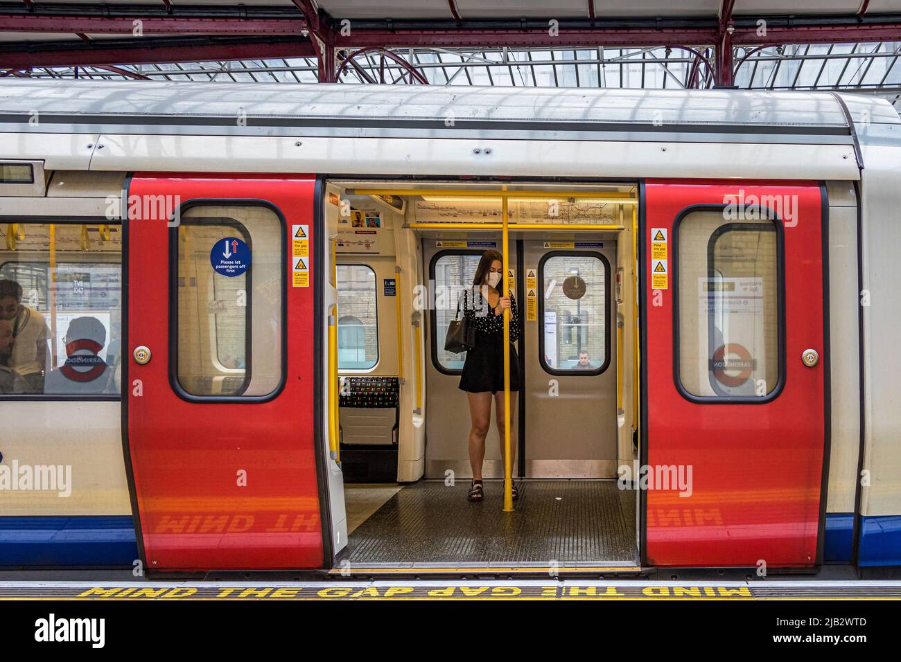 Una chica que lleva una máscara se sostiene sobre un pasamanos visto a través de las puertas abiertas del tren de metro en un tren subterráneo Circle Line en la estación Farringdon, Londres Foto de stock