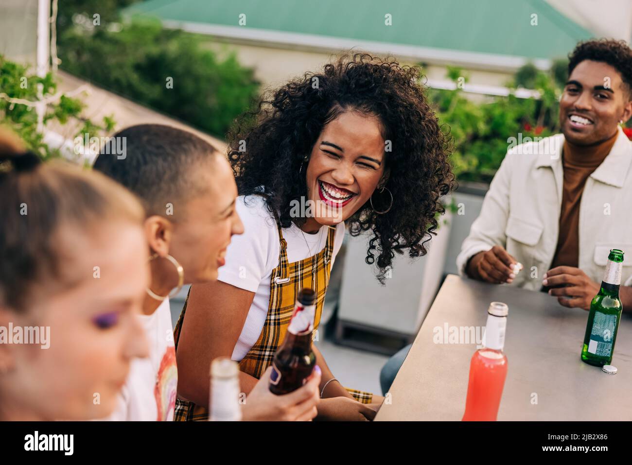 Feliz mujer joven riendo con sus amigos al aire libre. Grupo de jóvenes felices tomando algunas cervezas frías mientras que el pasar el rato en una azotea. Alegre amigo Foto de stock