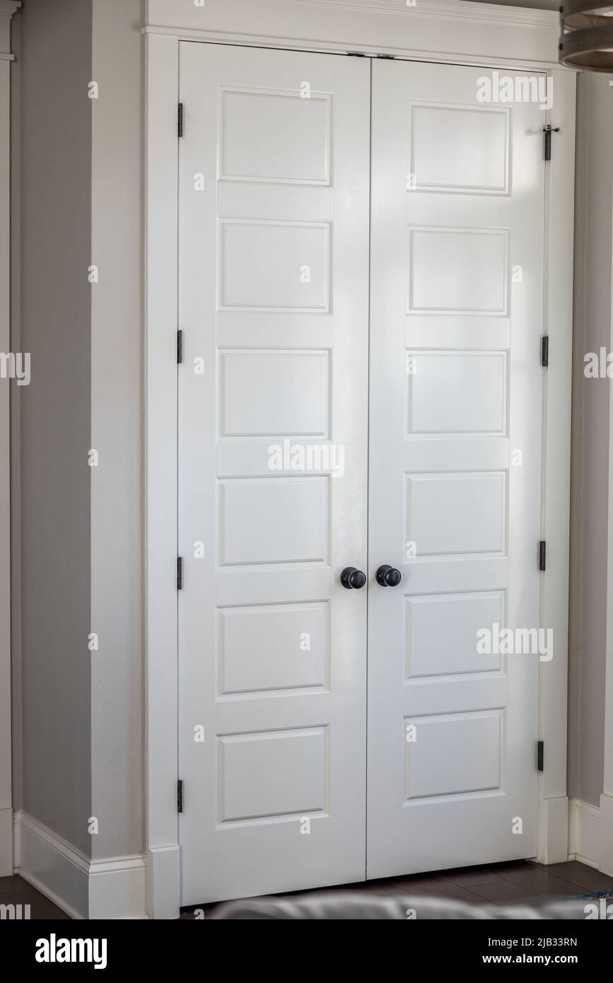 Un par o un conjunto de dos armarios de entrada pintados de blanco cerraron cinco puertas de paneles en una nueva casa de construcción con paredes greige Foto de stock