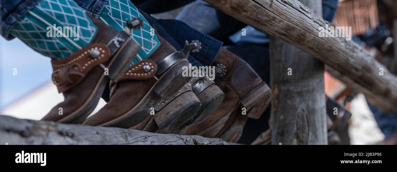 Botas de vaquero y espolones sentados en la valla corral viendo un rodeo Foto de stock